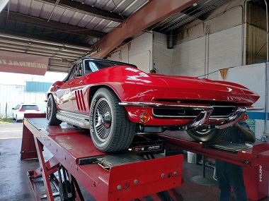 Red 1965 Corvette Sting Ray having its wheels aligned on a Hunter Engineering Alignment System inside the garage at Johnny Myers Discount Tires and Auto Repair